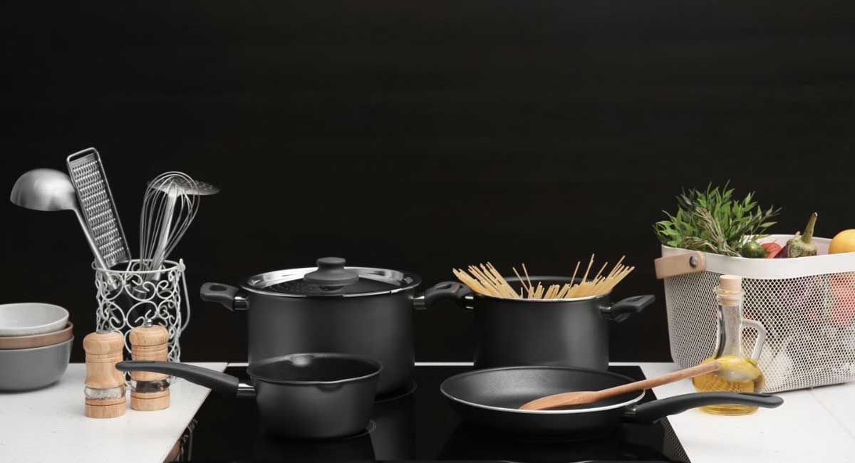 Polished stainless steel pots and pans arranged on a black glass cooktop in a modern kitchen.