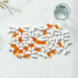 best probiotics — Overhead flat-lay of probiotic capsules arranged in neat rows on a pale stone surface beside a glass of water.