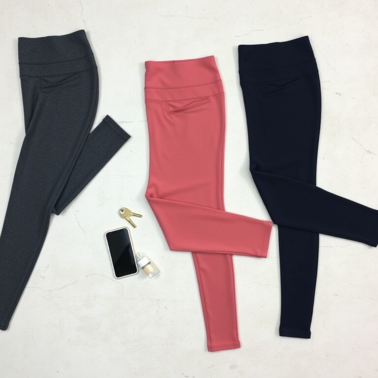 workout leggings review — Three pairs of high-rise workout leggings in charcoal, dusty rose, and navy flat-laid on concrete with a phone and key nearby.