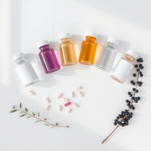 immune system vitamins — Six supplement bottles arranged on white marble with capsules and elderberry sprigs in soft natural light.